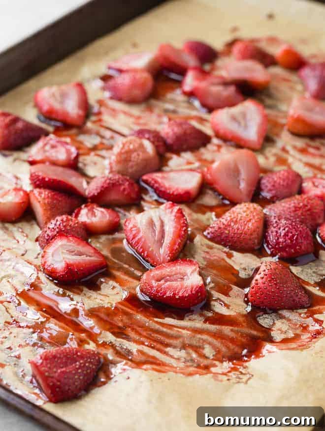 Image of roasted strawberries on a pan with parchment paper, their juices slightly caramelized. This process deepens their natural flavor.