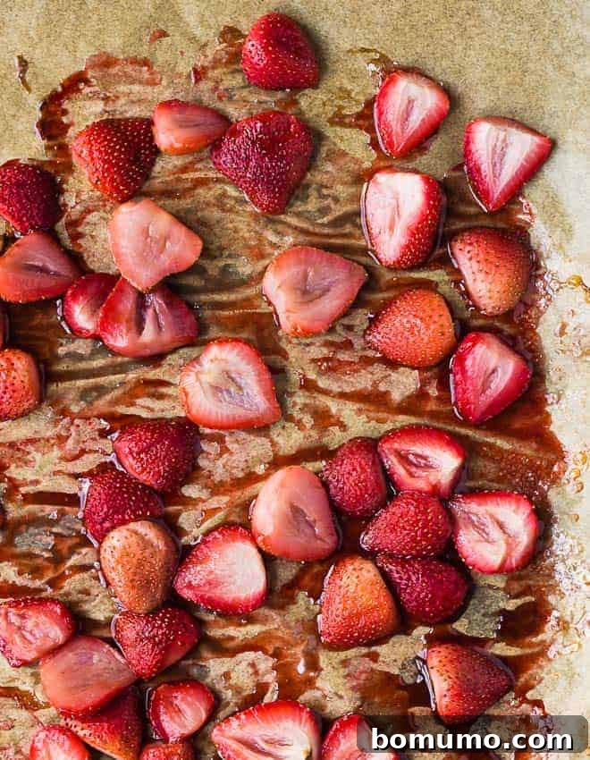 Roasted strawberries on a pan with parchment paper, glistening with caramelized syrup, ready to be a delicious topping.