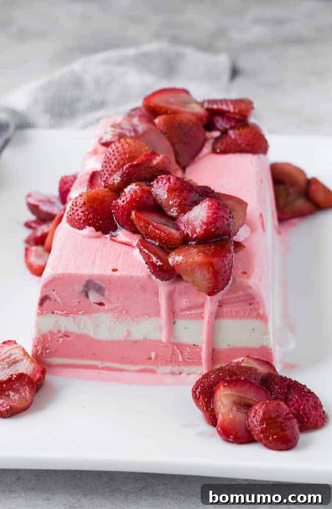 Close up of entire ice cream terrine on plate with roasted strawberries, highlighting the vibrant layers and appealing texture.