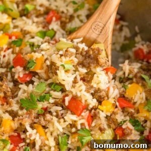 Close up of sausage, rice, and bell peppers in a skillet with a wooden spoon.
