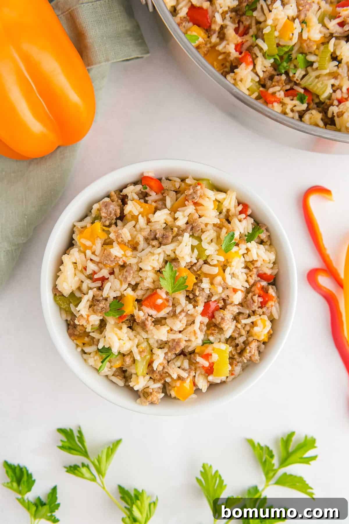 A beautifully presented white bowl filled with a generous portion of ground sausage, colorful bell peppers, and tender rice, elegantly garnished with fresh parsley.