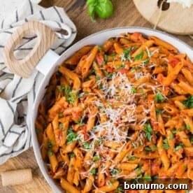 Overhead view of a pan of pasta with tomato sauce, fresh parsley, and grated cheese.