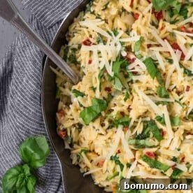 Overhead view of vegetarian orzo in a cast iron skillet, topped with fresh basil and parmesan cheese.