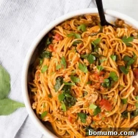 Overhead view of spaghetti and meat sauce in a white bowl, sprinkled with parsley.