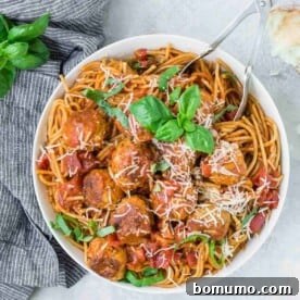 Overhead view of large white bowl full of spaghetti and meatballs, garnished with fresh basil.