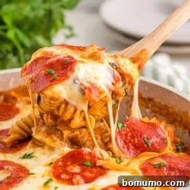 Pizza pasta being scooped from a pan with a wooden spoon.
