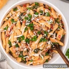Instant Pot pasta with sausage, spinach, tomatoes, in white bowl.