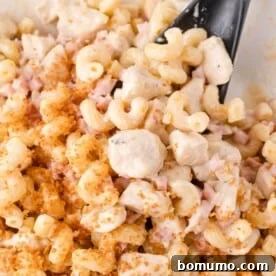 Close-up of creamy pasta with chunks of chicken, diced ham, breadcrumbs, and a black serving spoon.