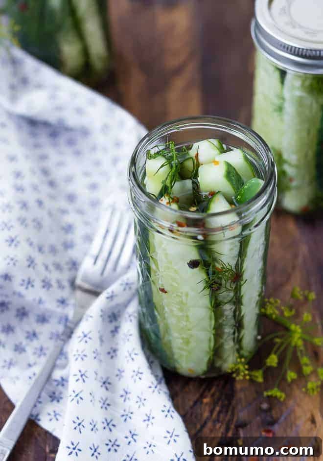 Pickles in slim glass canning jar without lid. Another jar in background.