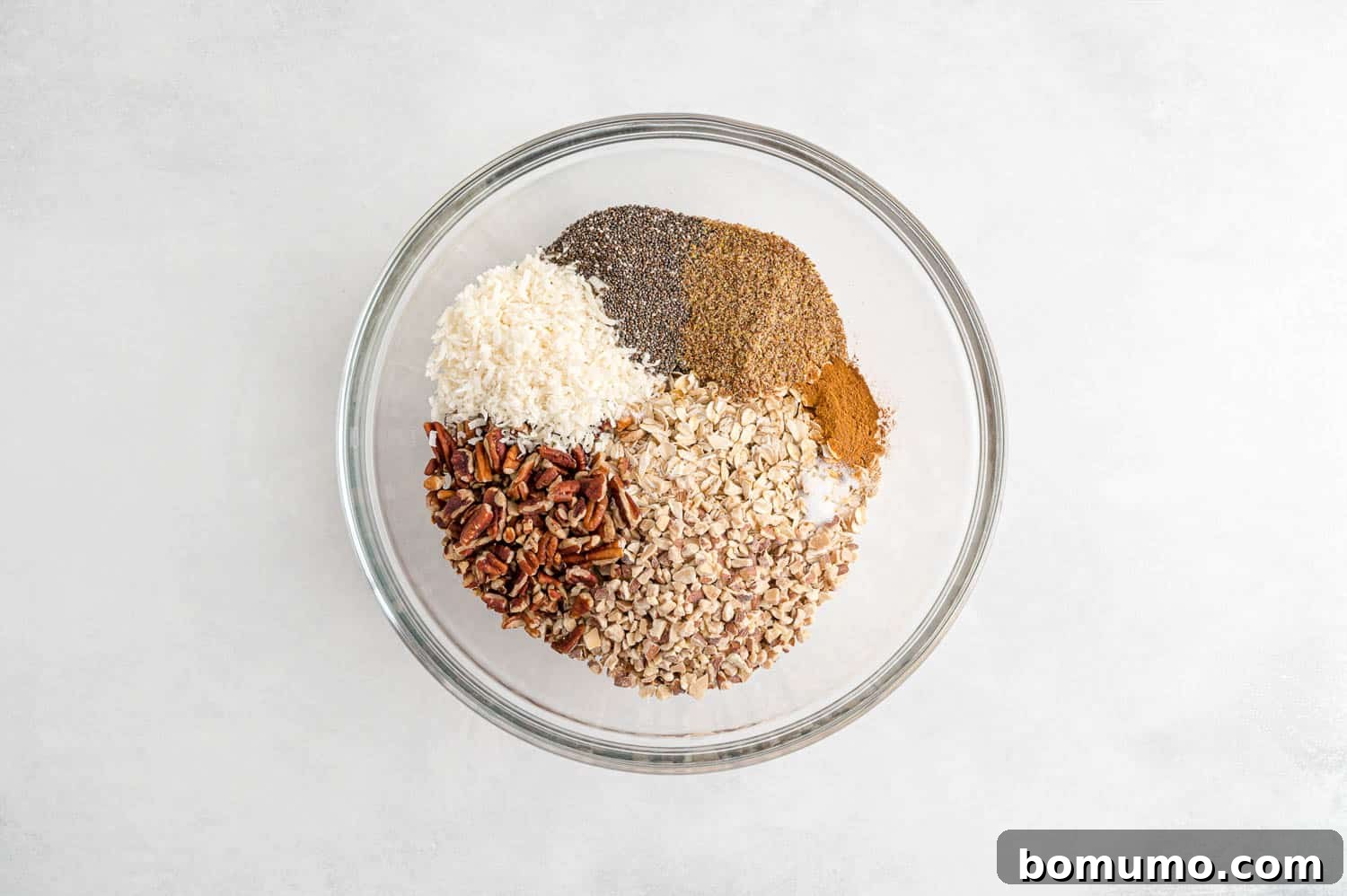 Unmixed dry ingredients for granola, including oats, nuts, and coconut, neatly arranged in a large mixing bowl, awaiting the next step.