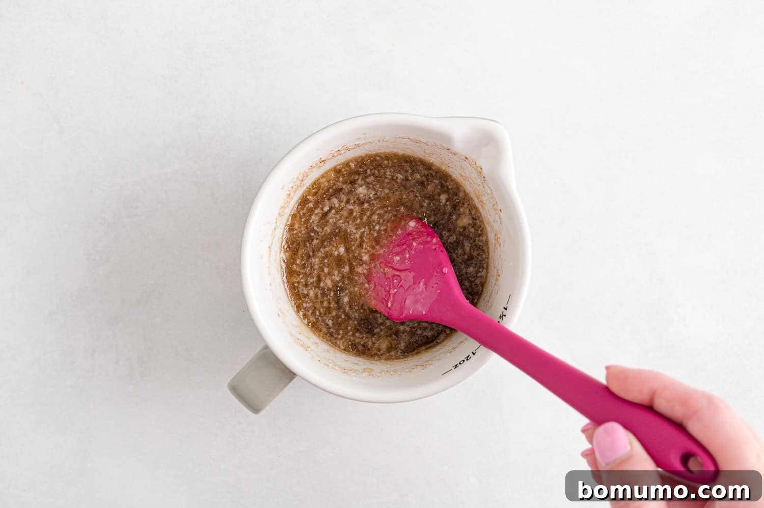 A spoon stirring wet ingredients in a bowl, showing the smooth, combined texture of honey, oil, and vanilla, ready to be added to the dry mix.