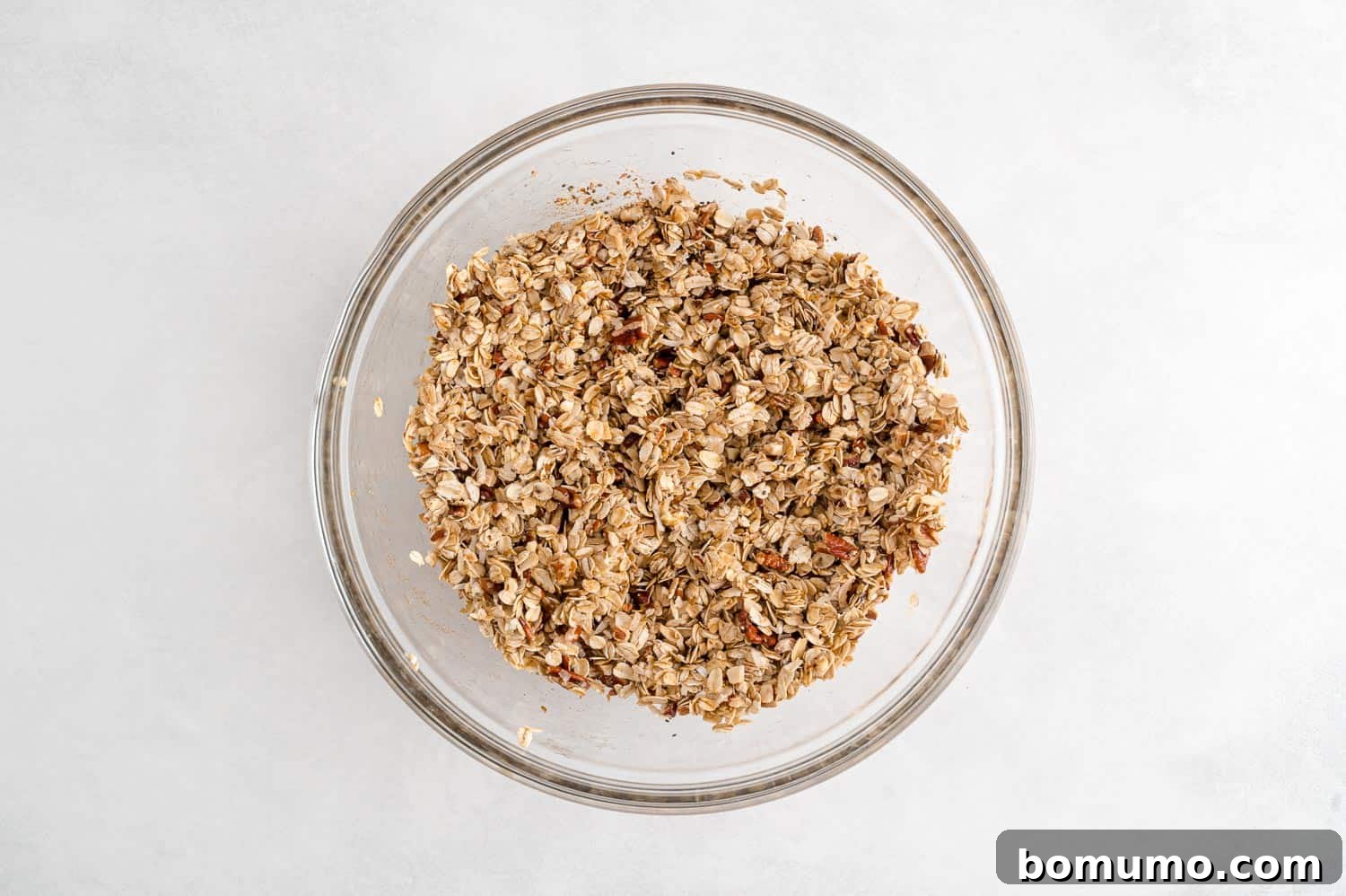 Unbaked granola mixture, perfectly coated with wet ingredients, resting in a bowl, showcasing its readiness for the oven.