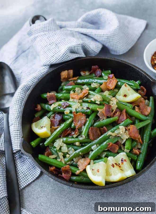 Green beans with bacon in a cast iron skillet, garnished with lemon wedges