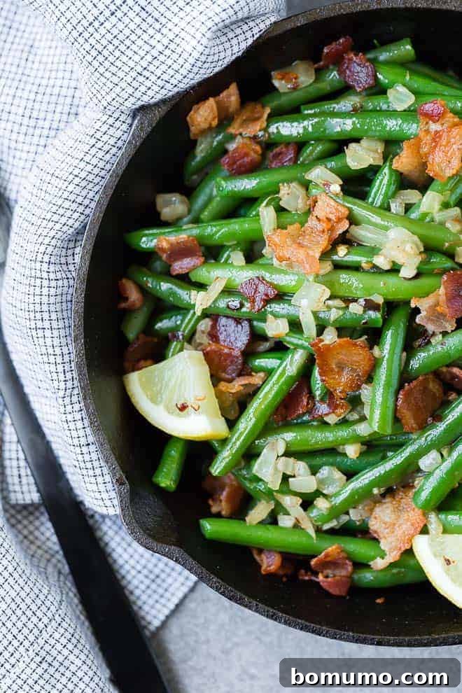 Overhead view of green beans and bacon in a black skillet.