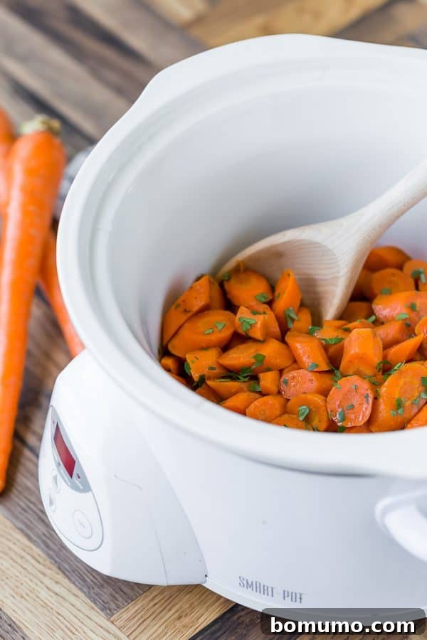 Slow cooker glazed carrots in a white slow cooker with a wooden spoon..
