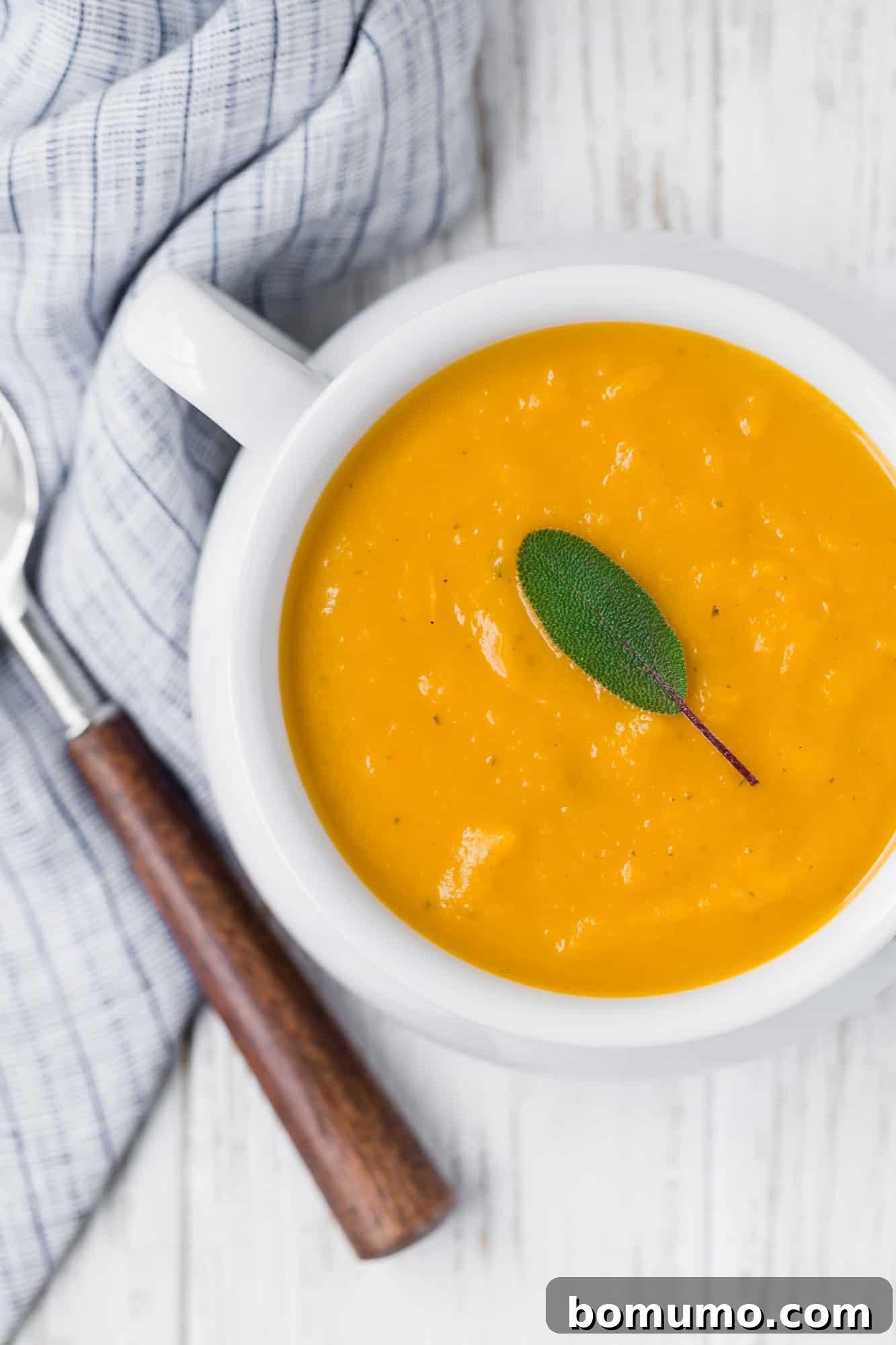 A beautifully presented bowl of creamy roasted butternut squash soup, garnished with fresh sage leaves.