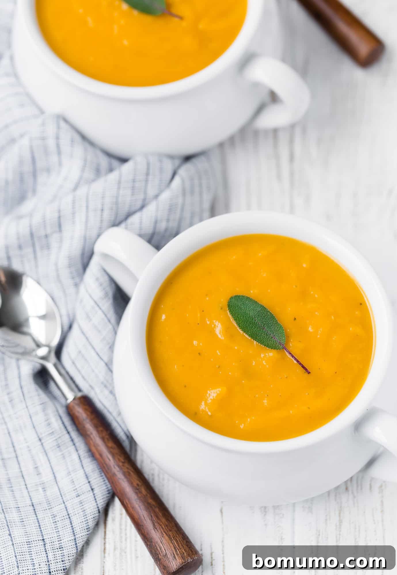 Close-up of vibrant orange butternut squash soup with a single sage leaf, highlighting its smooth texture.
