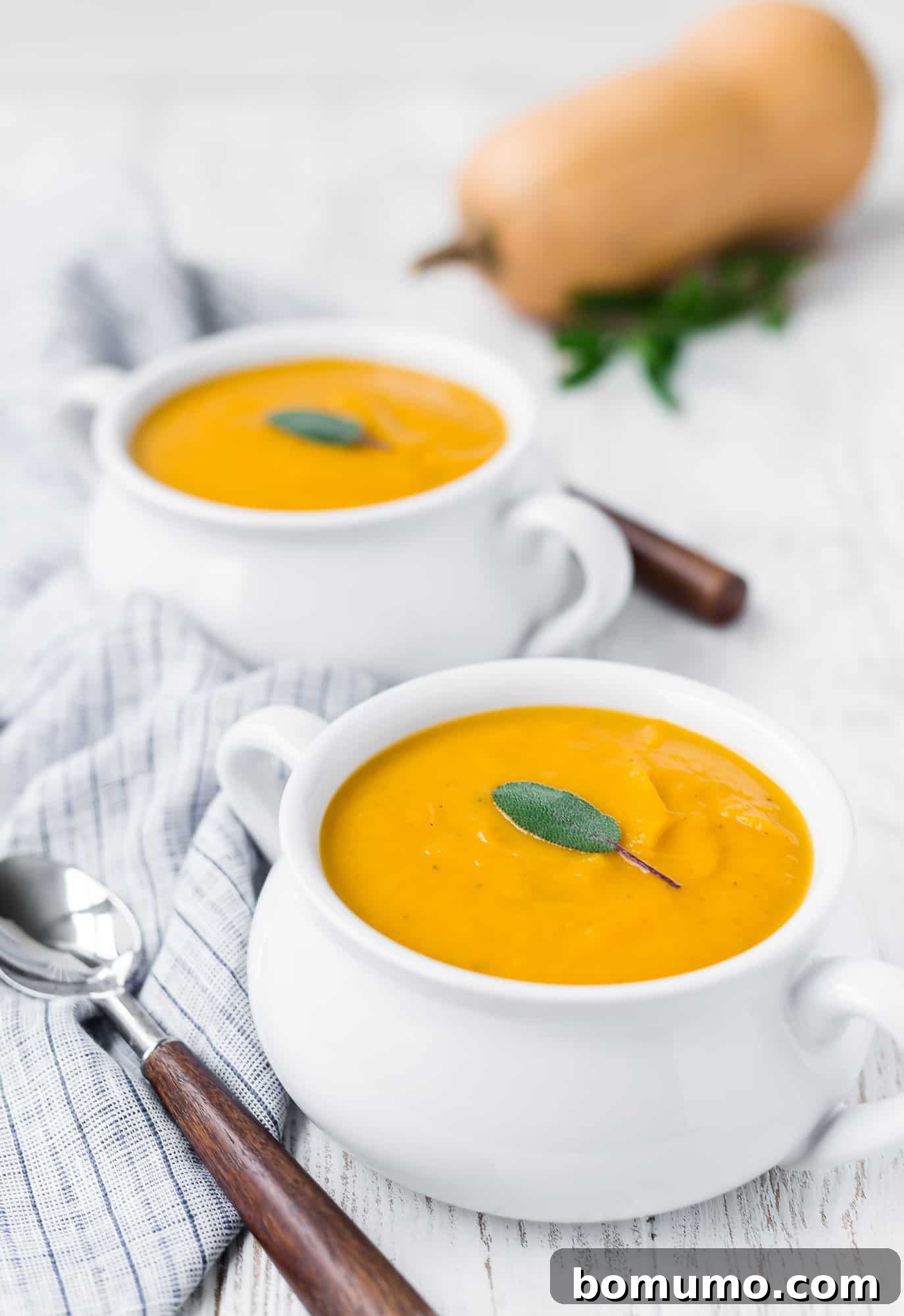 Two cozy bowls of butternut squash soup, garnished with sage, ready to be served.