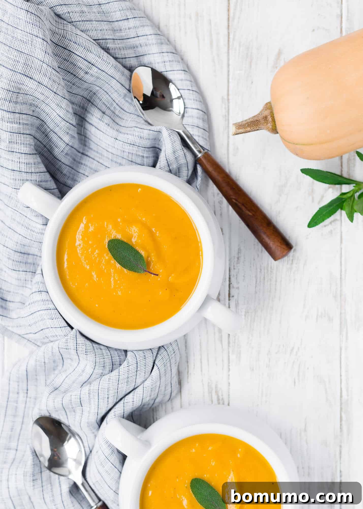 Overhead shot of two bowls of butternut squash soup, garnished with sage, showcasing its inviting texture.