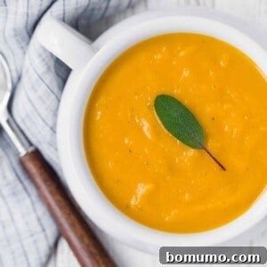 Creamy butternut squash soup in a white bowl, topped with a fresh sage leaf.