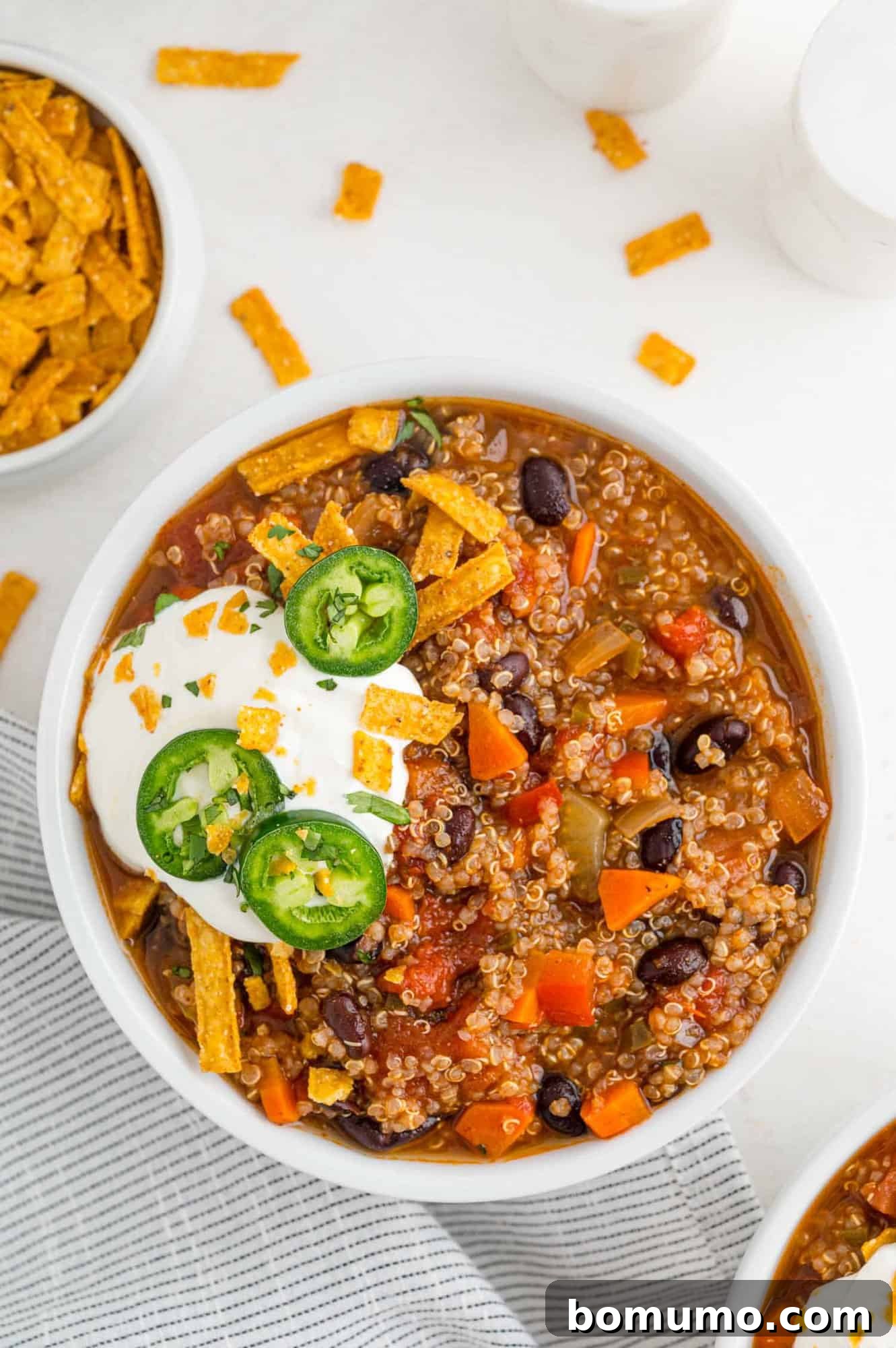 A vibrant bowl of vegetarian quinoa chili, beautifully garnished with a dollop of sour cream and a slice of fresh jalapeño, showcasing its rich texture and color.