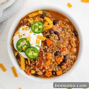 Round bowl of quinoa chili with black beans, garnished with sour cream and jalapeno.
