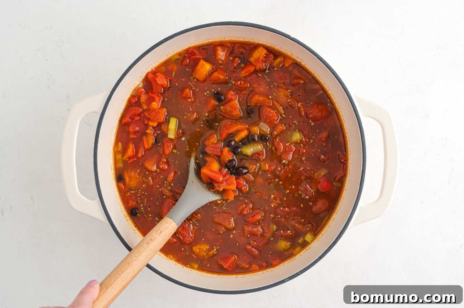 A vibrant pot of chili before the quinoa is added, showcasing the rich tomato base, black beans, and tender vegetables simmering together.