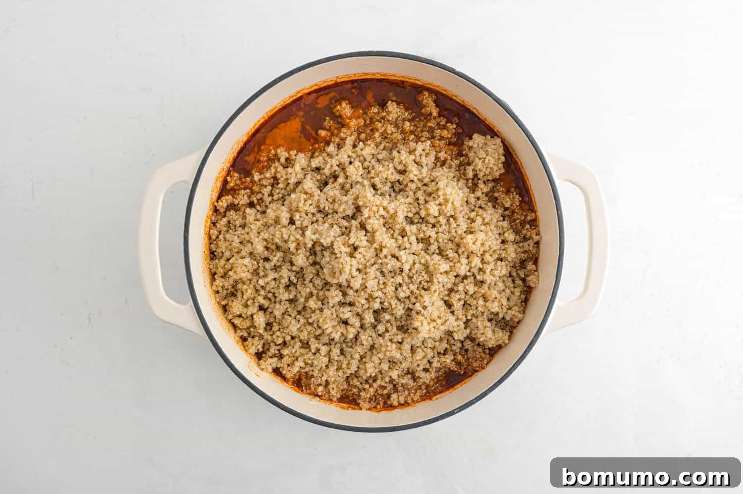 Cooked quinoa, light and fluffy, visibly added to the top of the simmering chili in a large pot, ready to be stirred in and absorbed.