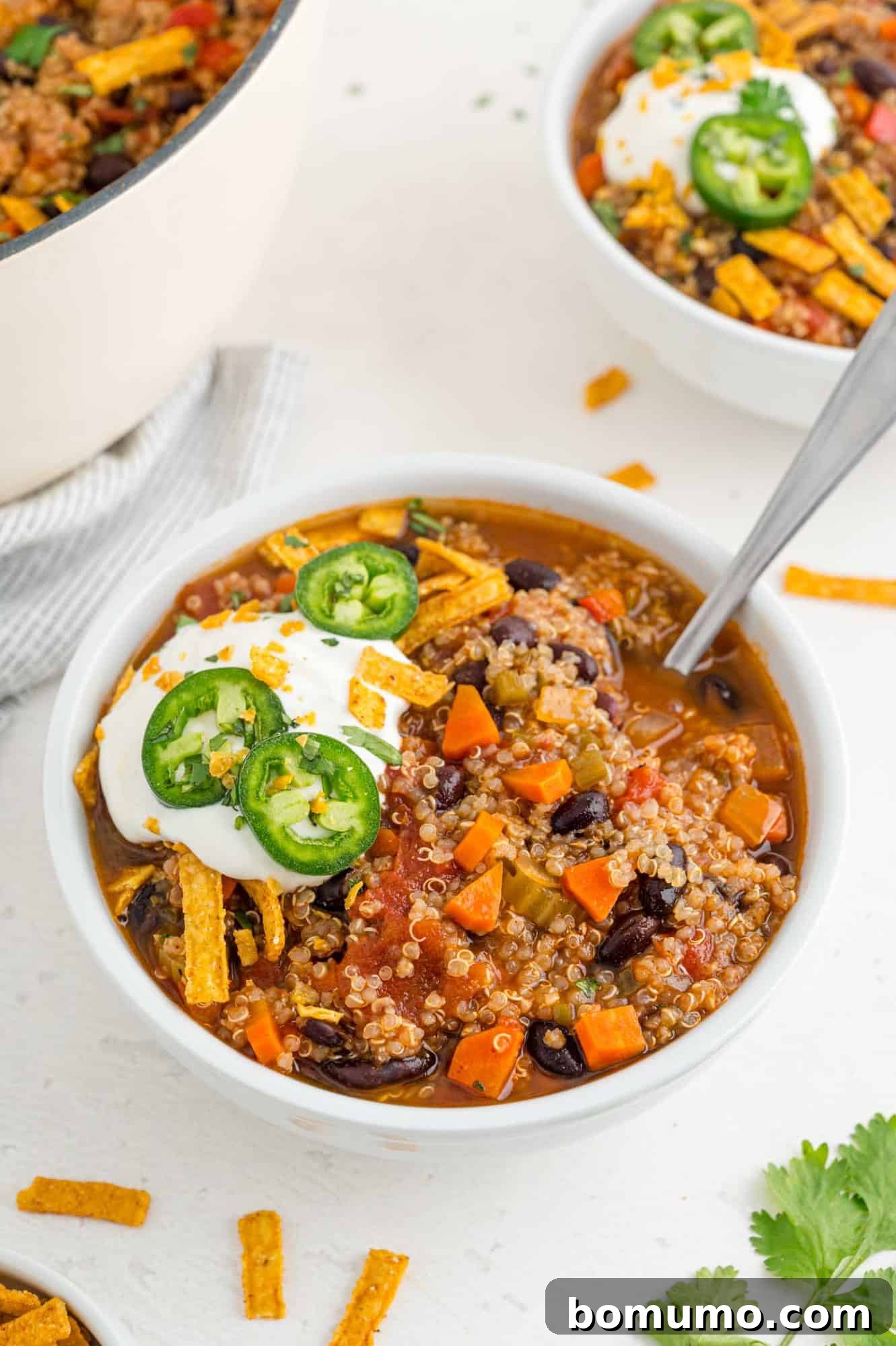 A beautifully presented white bowl filled with vegetarian quinoa chili, topped generously with sour cream, shredded cheese, and fresh green onions, inviting a delicious spoonful.