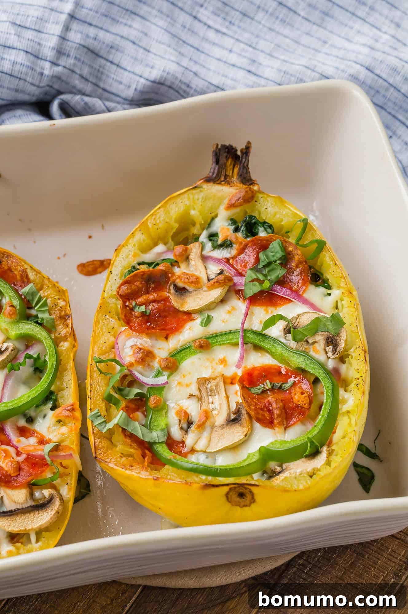 Golden-baked spaghetti squash halves brimming with an assortment of colorful pizza toppings, ready for the broiler.