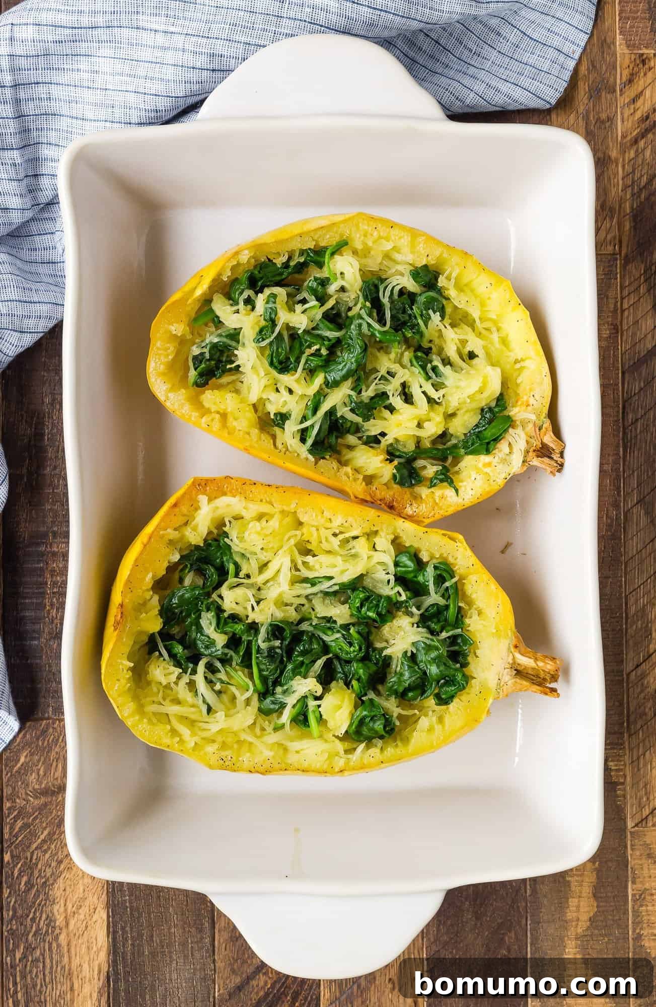 Perfectly cooked spaghetti squash halves, with vibrant green spinach leaves gently nestled among the golden squash strands, ready for further layering.