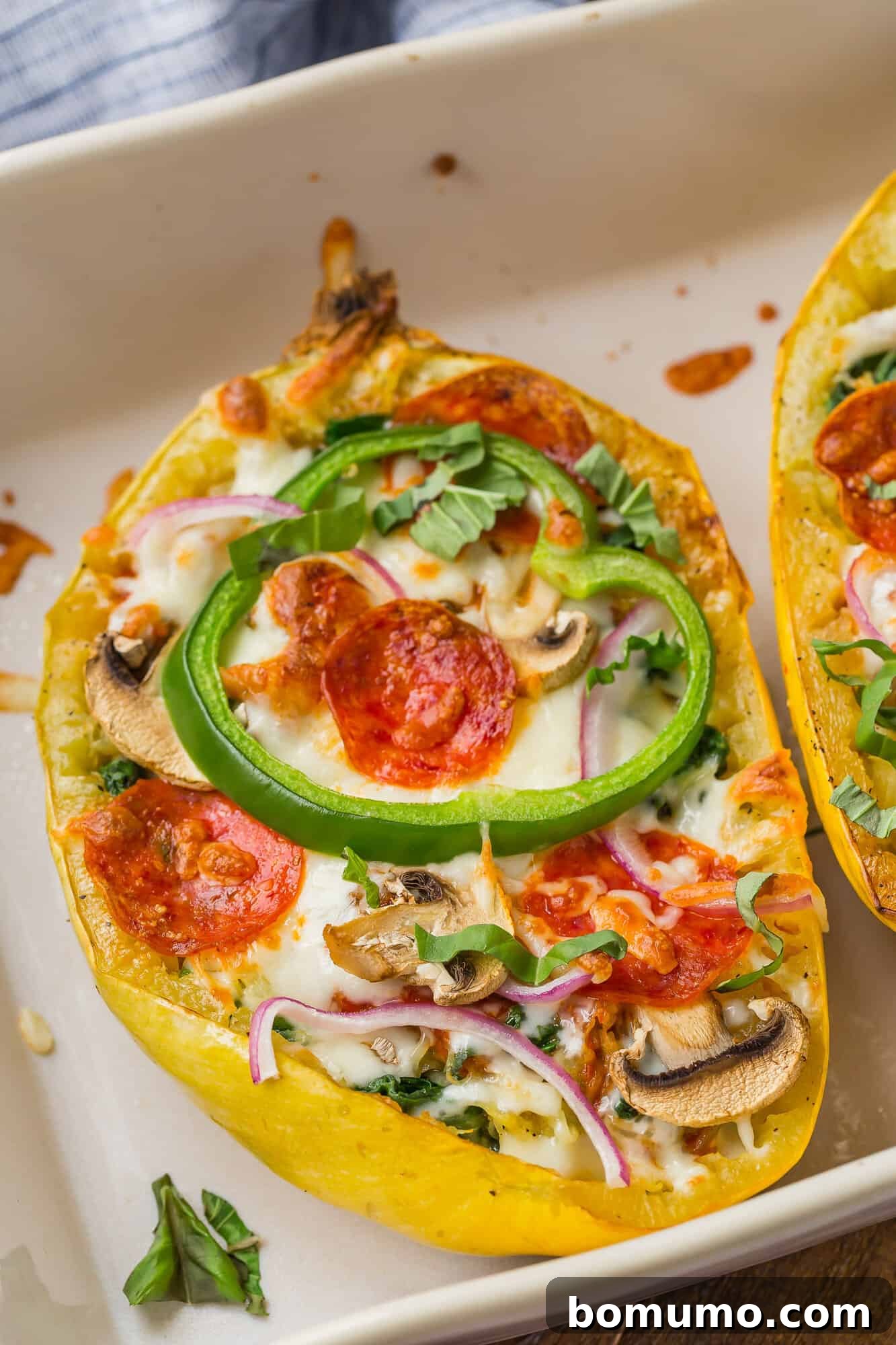 Several halves of pizza stuffed spaghetti squash nestled in a baking dish, showcasing their golden-brown melted cheese and colorful toppings, ready to be served.