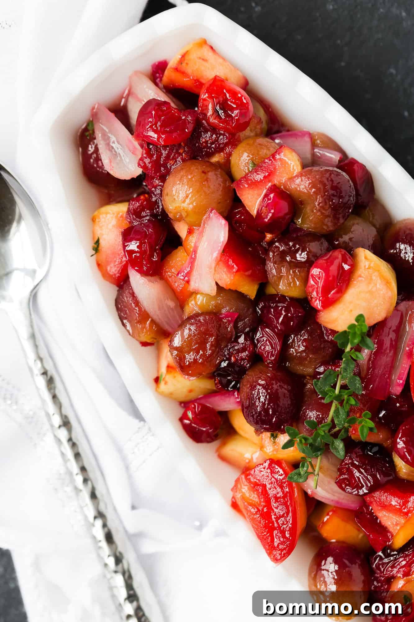 Close-up of roasted cranberry sauce with grapes and shallots in a rustic bowl, garnished with fresh thyme.