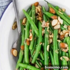 Green beans almondine on a white plate, garnished with toasted almonds.