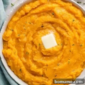 Mashed butternut squash in a large bowl, topped with butter and thyme sprigs.