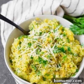 Spaghetti squash in a white bowl, generously sprinkled with fresh green parsley and grated white Parmesan cheese.