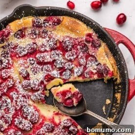 A festive cranberry clafoutis with a slice removed, revealing its custard-like texture and bright cranberries.
