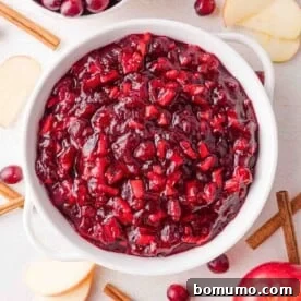 Apple cinnamon cranberry sauce in a white bowl, viewed from above, garnished with cinnamon sticks.