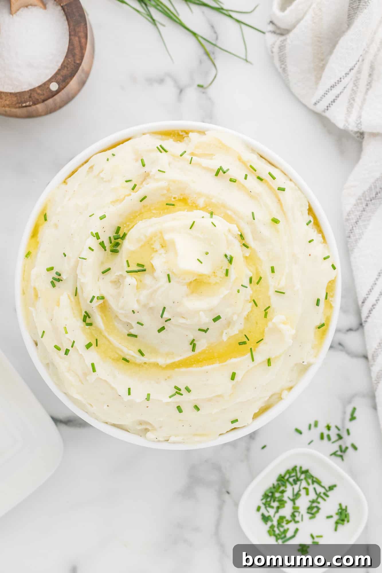 Overhead view of instant pot mashed potatoes in white bowl, garnished with fresh herbs.