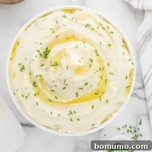 Instant pot mashed potatoes in a white serving bowl, garnished with fresh herbs.
