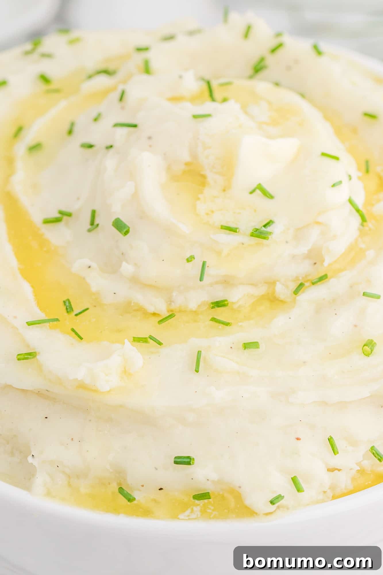 Mashed potatoes topped with melting butter and fresh chives, ready to serve.