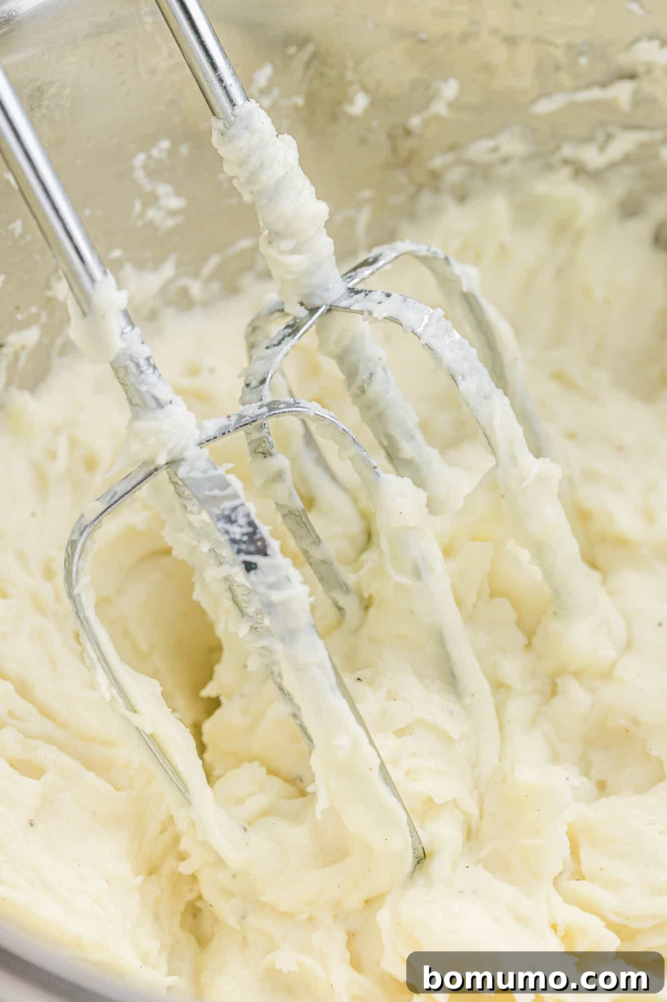 Mashed potatoes being whipped to a creamy consistency with an electric hand mixer.