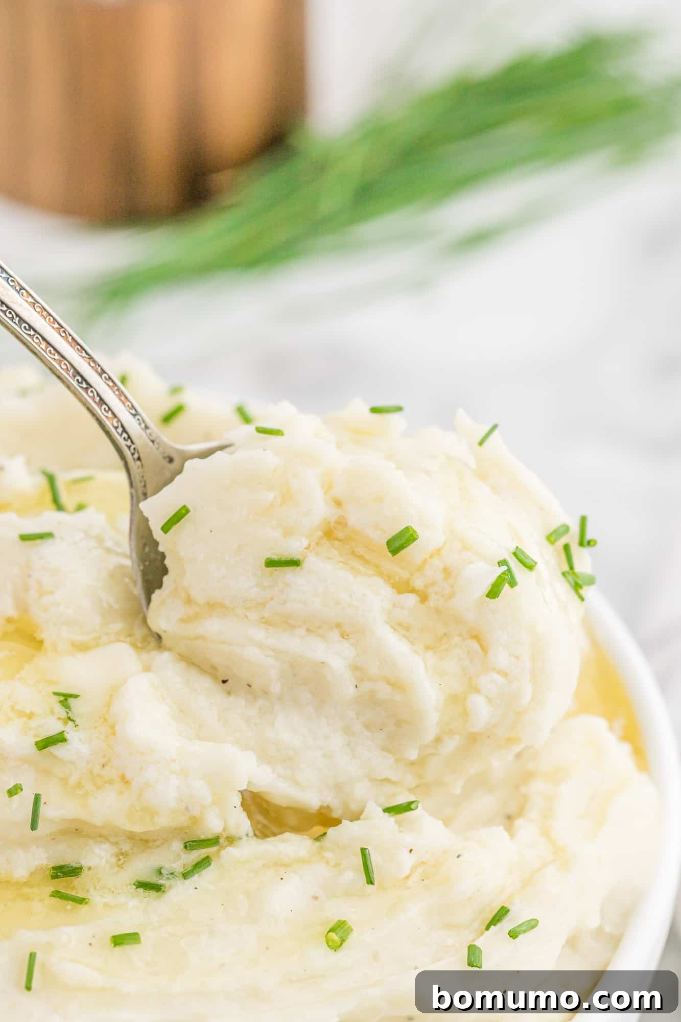 Close-up of creamy mashed potatoes on a serving spoon, garnished with chives.