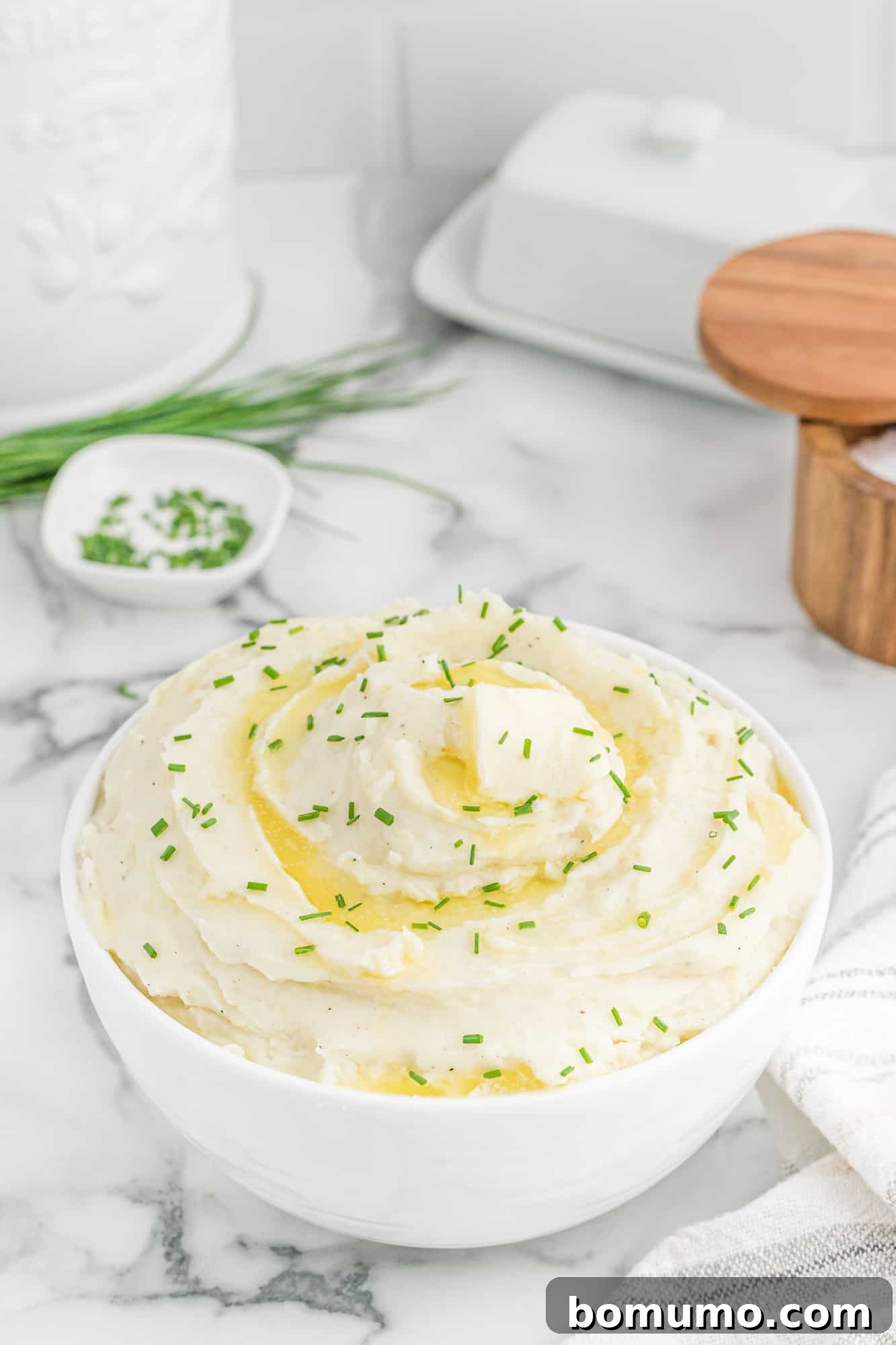 Creamy mashed potatoes topped with melting butter and fresh chives, in a white serving bowl.
