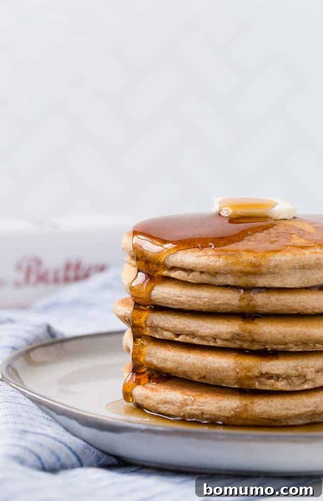 Image of a beautiful stack of golden whole wheat pancakes topped with a melting pat of butter and generous maple syrup drizzle.