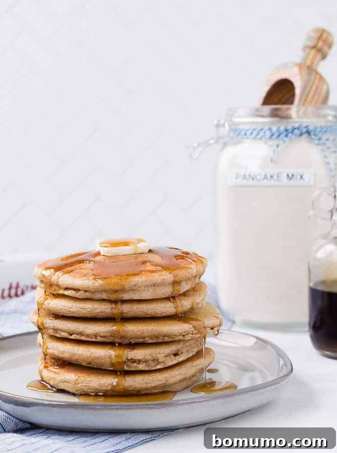 A stack of golden pancakes on a white plate, generously topped with a pat of melting butter and glistening maple syrup.