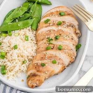 Sliced cooked chicken breast with sesame seeds and green onion garnish.