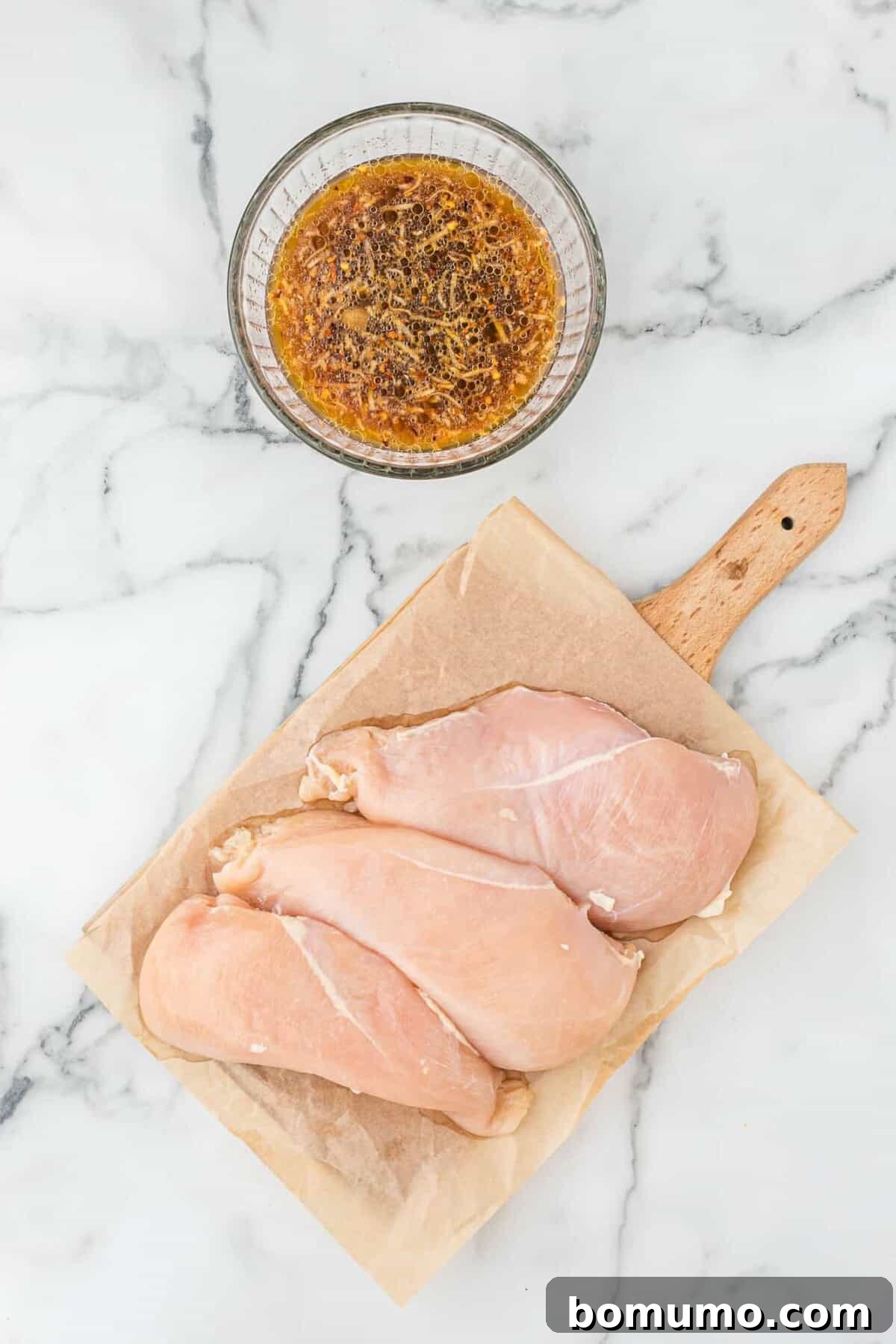 Raw chicken in a dish, alongside a bowl of freshly prepared Asian marinade.