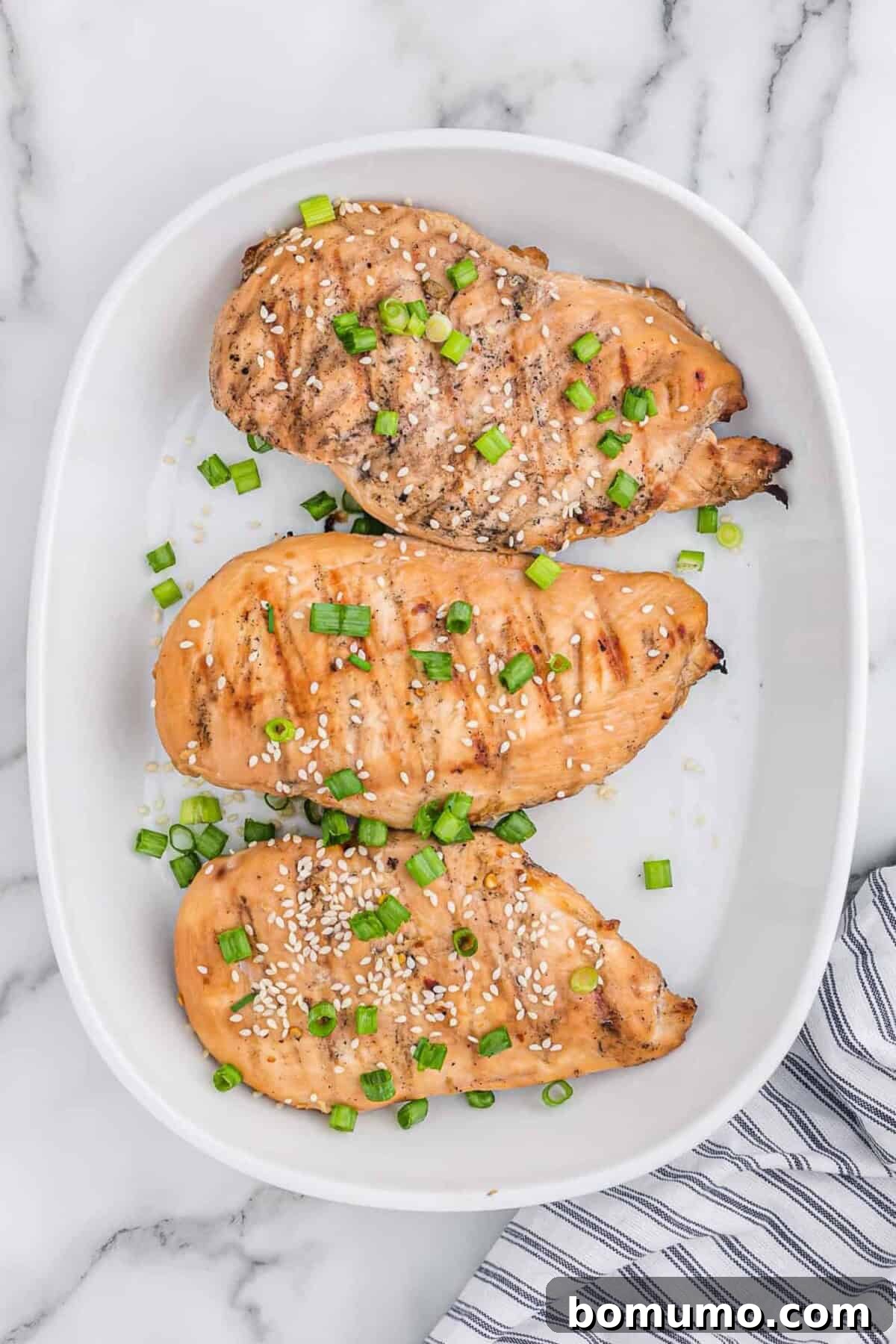 Three perfectly grilled chicken breasts on a pristine white plate.