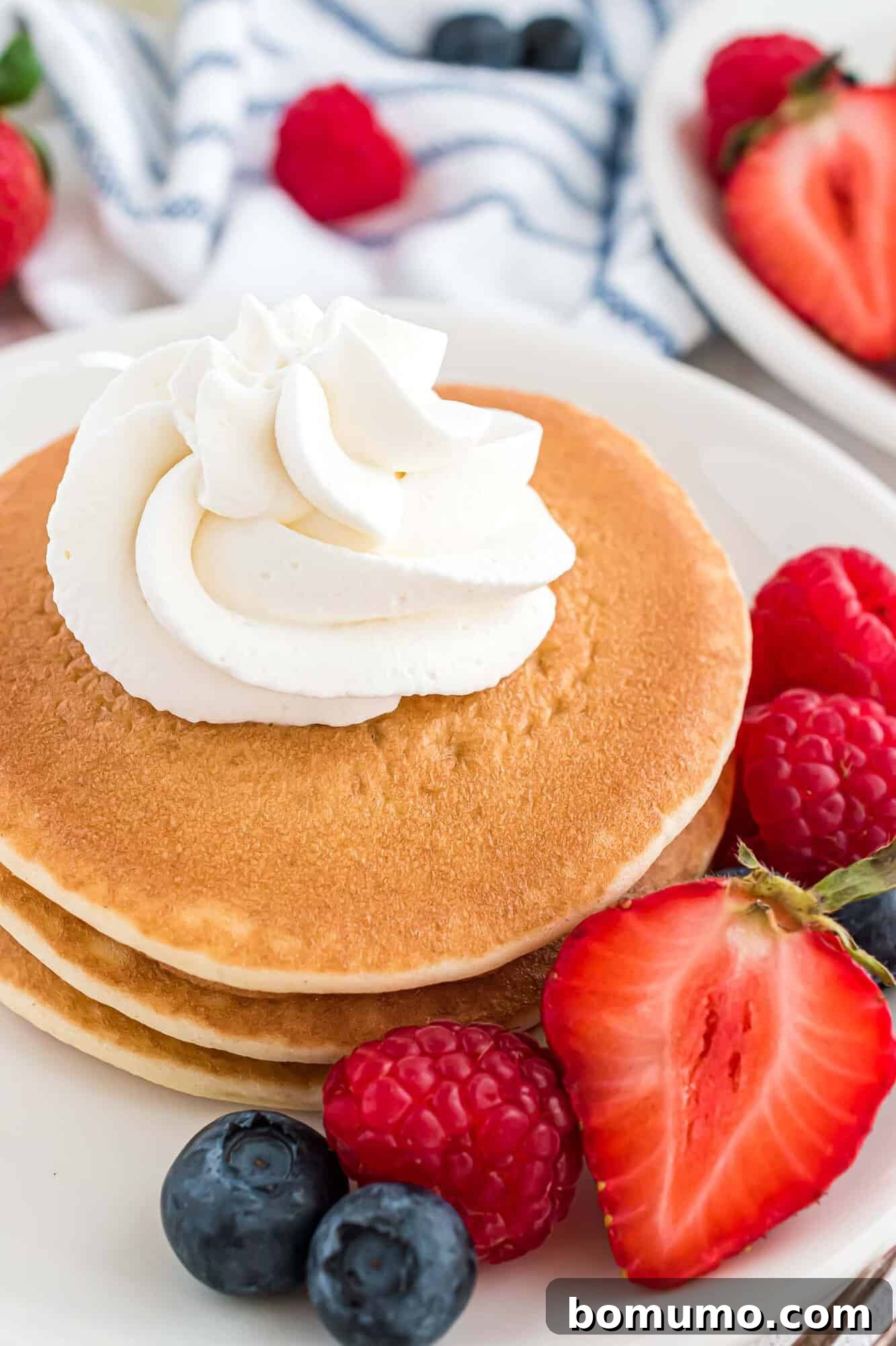 Whipped cream on a short stack of pancakes, making a simple breakfast feel gourmet.